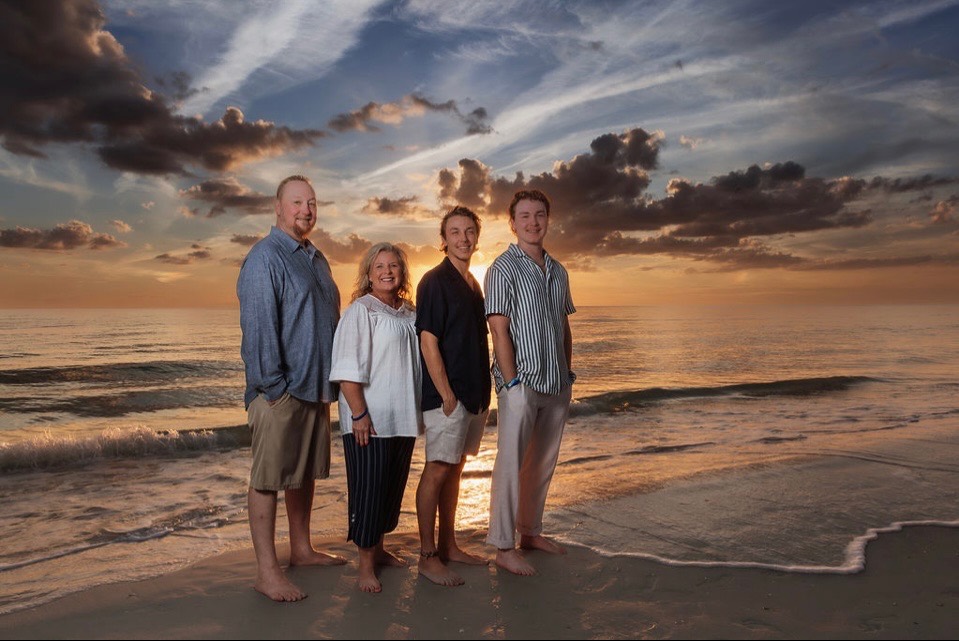 Chris and his family standing together on a beach at sunset.
