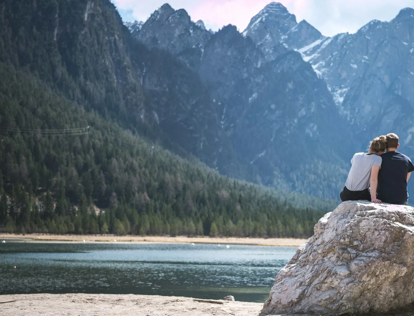 Two people sitting together beside a mountain lake.
